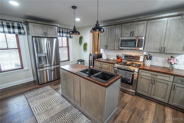 kitchen with sink, wooden counters, appliances with stainless steel finishes, a center island with sink, and decorative light fixtures