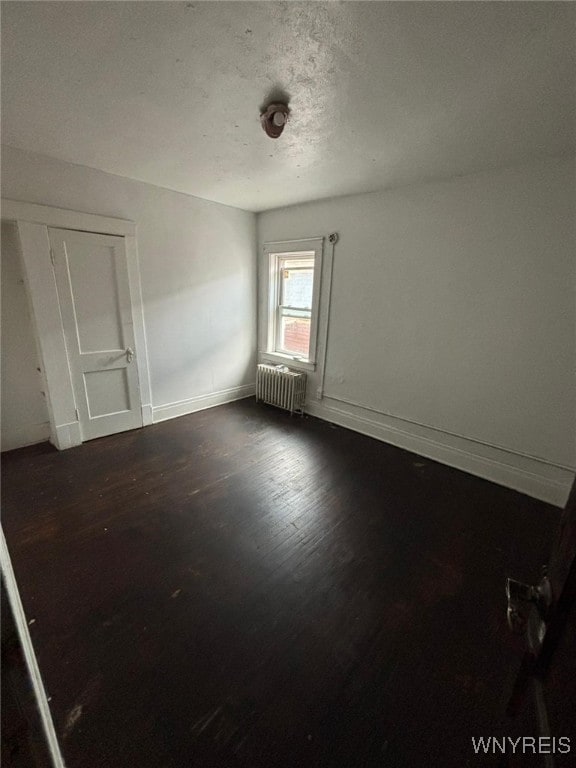 unfurnished room featuring dark hardwood / wood-style flooring, radiator, and a textured ceiling