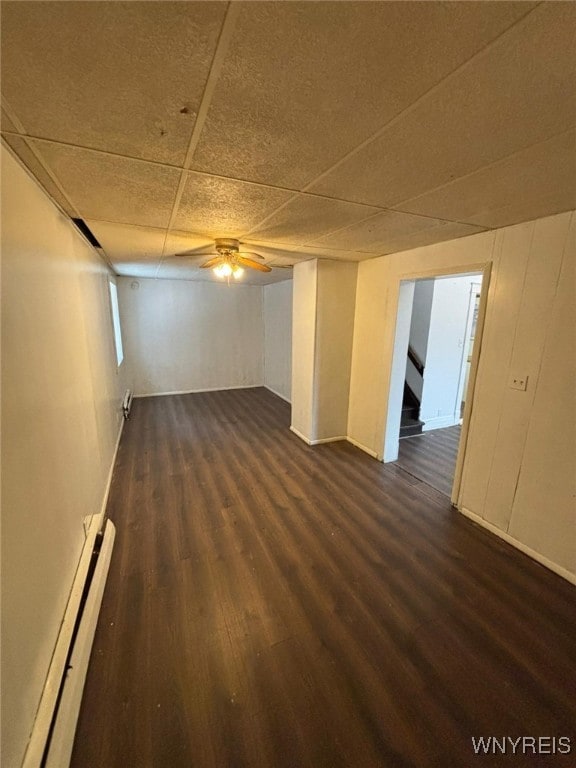 basement with baseboard heating, a paneled ceiling, dark hardwood / wood-style flooring, and ceiling fan