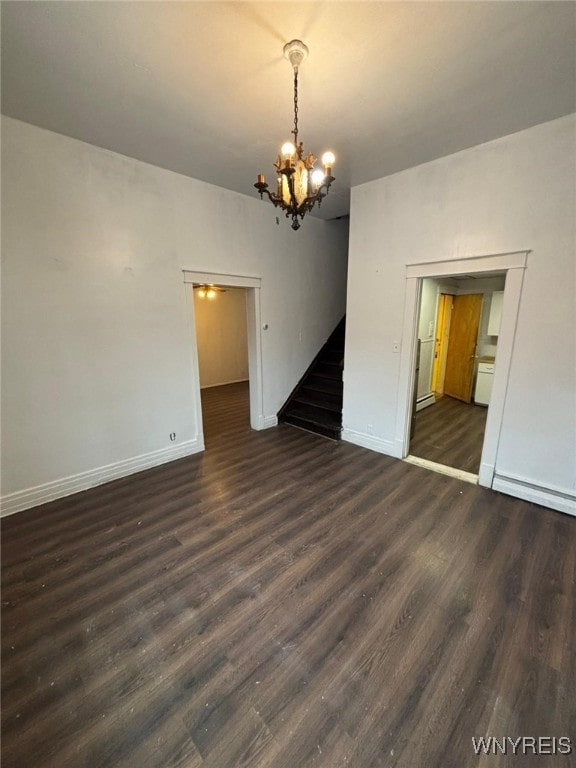 unfurnished room featuring an inviting chandelier, dark wood-type flooring, and baseboard heating