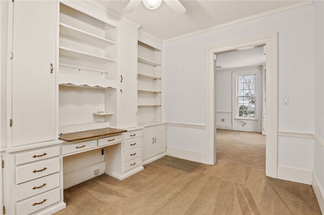 unfurnished office with ceiling fan, light colored carpet, ornamental molding, and built in desk