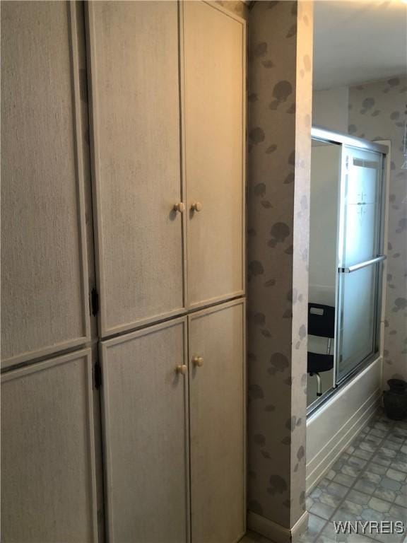 bathroom featuring combined bath / shower with glass door and wallpapered walls