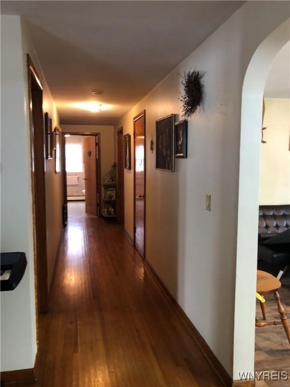 hallway featuring baseboards, arched walkways, and hardwood / wood-style floors