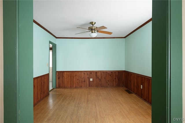 spare room with ceiling fan, ornamental molding, wooden walls, and light hardwood / wood-style floors