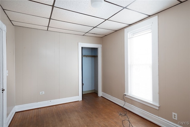 unfurnished bedroom featuring a paneled ceiling, wood-type flooring, and a closet