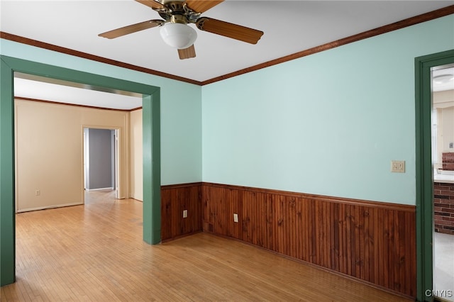 empty room featuring crown molding, ceiling fan, wooden walls, and light hardwood / wood-style flooring