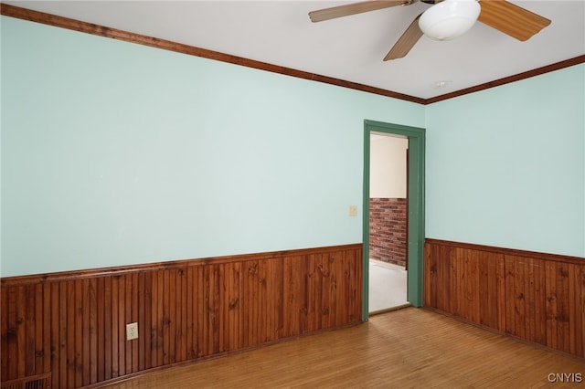 unfurnished room with crown molding, ceiling fan, wooden walls, and light hardwood / wood-style floors