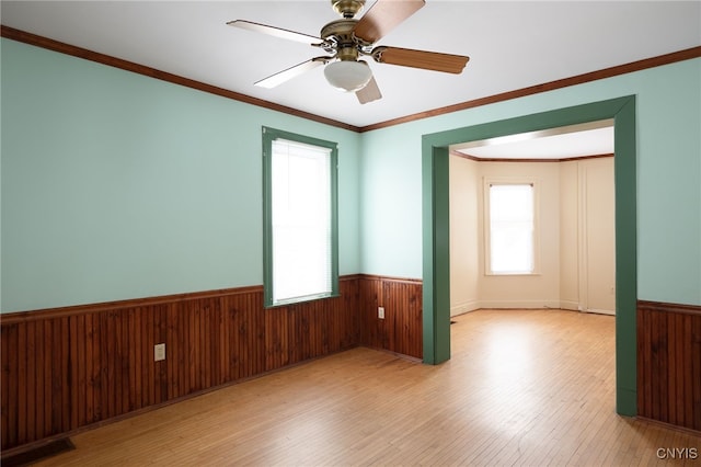 unfurnished room featuring crown molding, ceiling fan, light wood-type flooring, and wood walls