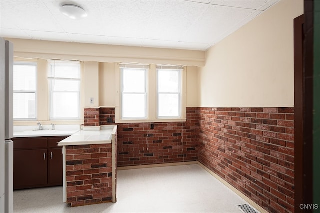 bar with brick wall, sink, and dark brown cabinetry