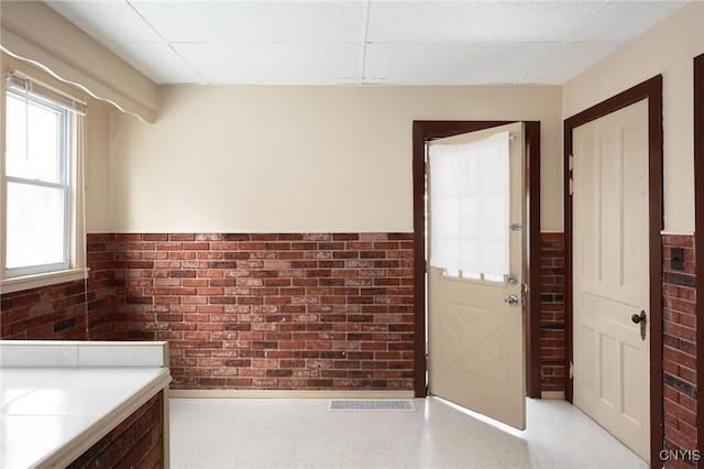 interior space with a paneled ceiling and brick wall