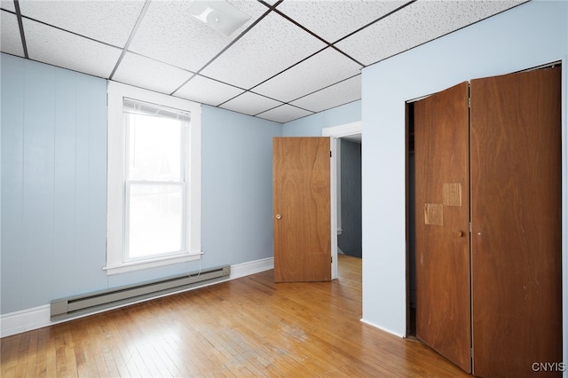 unfurnished bedroom with a baseboard radiator, a drop ceiling, light hardwood / wood-style floors, and a closet