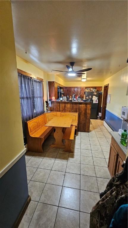 interior space with a ceiling fan, a peninsula, light tile patterned floors, and freestanding refrigerator
