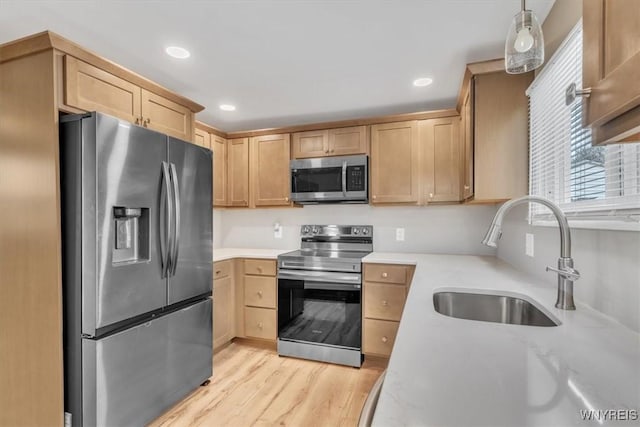 kitchen with stainless steel appliances, sink, light brown cabinets, and decorative light fixtures