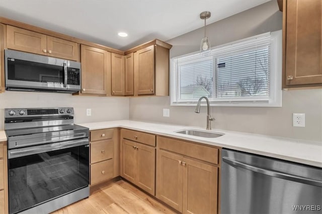 kitchen featuring sink, light hardwood / wood-style flooring, hanging light fixtures, and appliances with stainless steel finishes