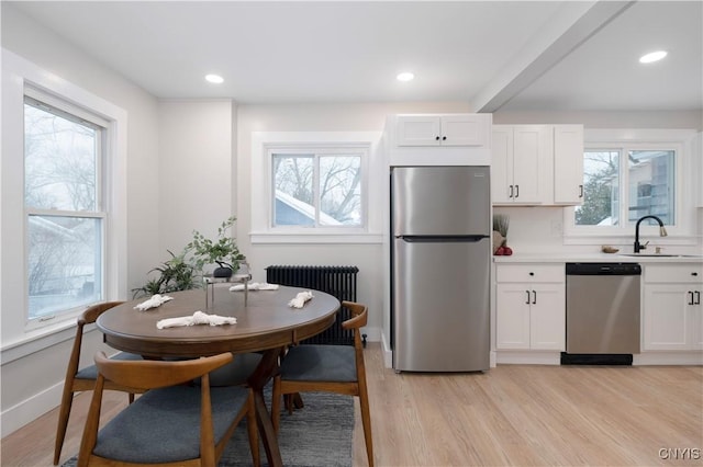 kitchen with sink, white cabinetry, light wood-type flooring, appliances with stainless steel finishes, and radiator