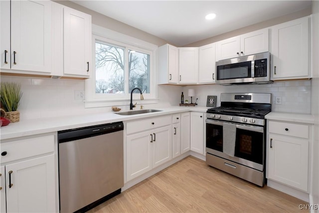 kitchen with sink, appliances with stainless steel finishes, white cabinetry, decorative backsplash, and light wood-type flooring