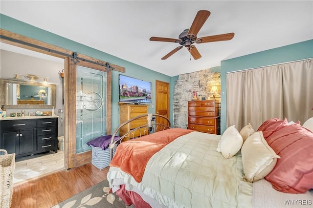 bedroom featuring a barn door, ceiling fan, and light hardwood / wood-style flooring