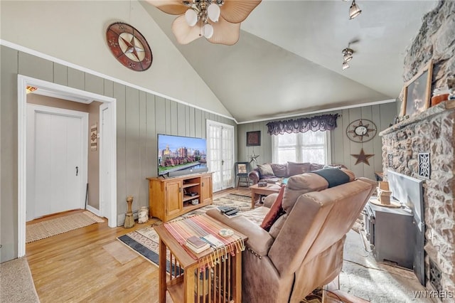 living room featuring a stone fireplace, high vaulted ceiling, rail lighting, ceiling fan, and light wood-type flooring