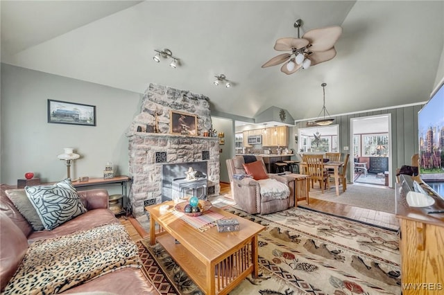 living room with lofted ceiling, a stone fireplace, and ceiling fan