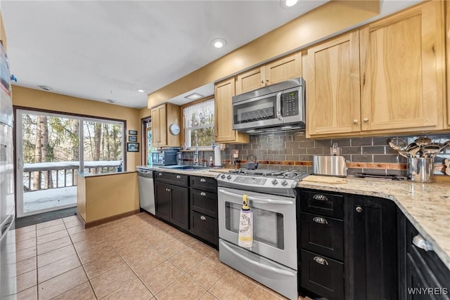 kitchen with sink, light tile patterned floors, stainless steel appliances, light stone countertops, and decorative backsplash