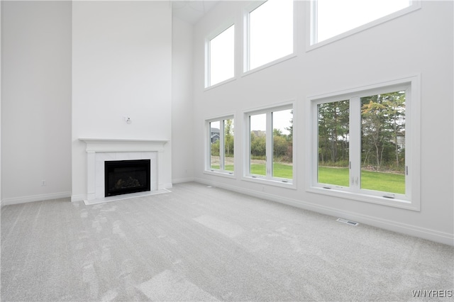 unfurnished living room with light carpet, a tiled fireplace, and a towering ceiling