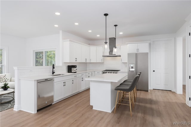 kitchen with wall chimney range hood, sink, white cabinetry, stainless steel appliances, and a center island