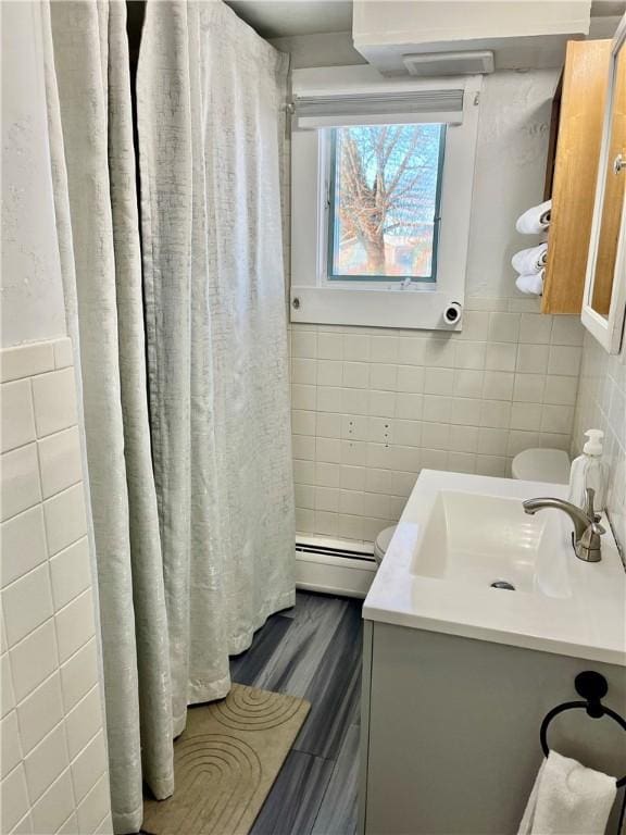 bathroom with vanity, wood-type flooring, a baseboard heating unit, and tile walls