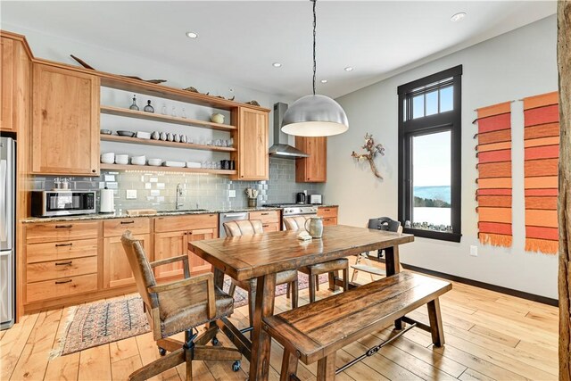 kitchen with light wood-type flooring, a sink, backsplash, appliances with stainless steel finishes, and wall chimney exhaust hood