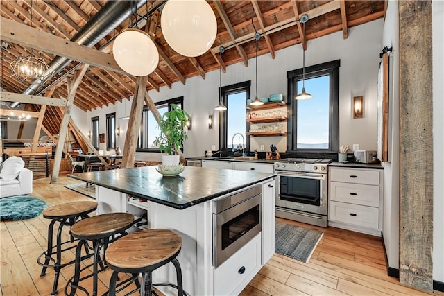 kitchen featuring light wood-type flooring, dark countertops, white cabinetry, appliances with stainless steel finishes, and vaulted ceiling with beams