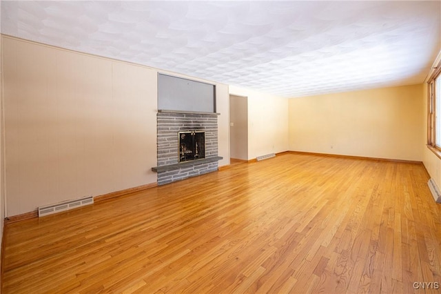 unfurnished living room featuring a fireplace, a textured ceiling, and light wood-type flooring