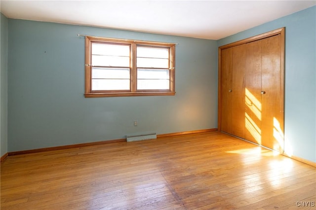 unfurnished bedroom with a baseboard heating unit, light hardwood / wood-style floors, and a closet