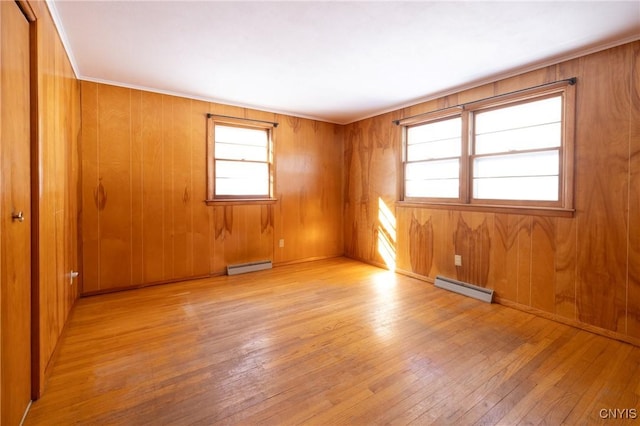 unfurnished room featuring a baseboard radiator, wood walls, and light wood-type flooring