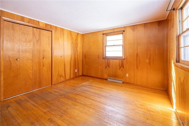 unfurnished bedroom featuring wood walls, crown molding, light wood-type flooring, a closet, and a baseboard heating unit