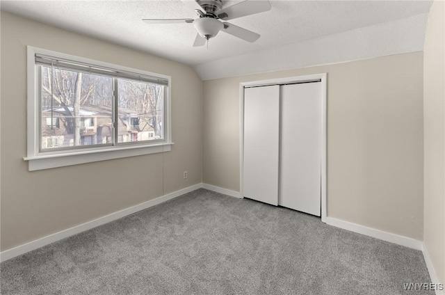 unfurnished bedroom with lofted ceiling, light colored carpet, a textured ceiling, a closet, and ceiling fan