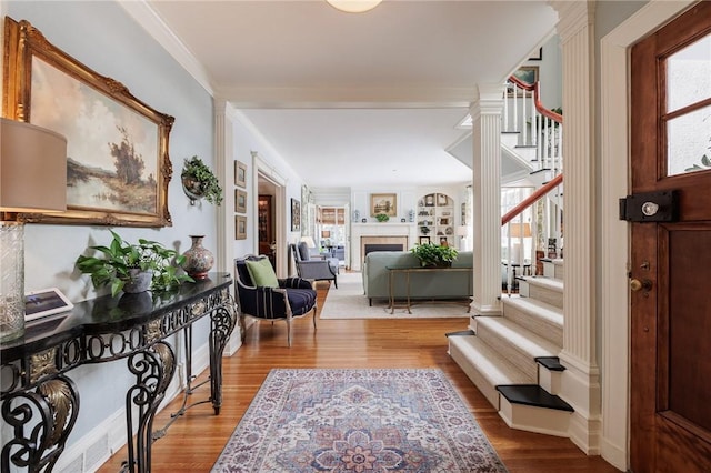 entrance foyer featuring ornate columns, ornamental molding, a wealth of natural light, and light wood-type flooring