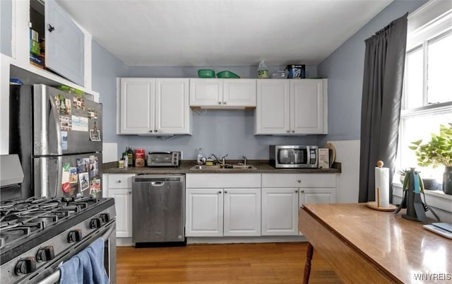 kitchen with sink, light wood-type flooring, white cabinets, and appliances with stainless steel finishes