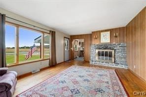 living room featuring wood-type flooring, a stone fireplace, and wooden walls