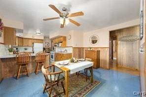 dining room with concrete floors, ceiling fan, and wood walls