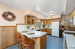 kitchen with a breakfast bar area, wood walls, white appliances, and kitchen peninsula