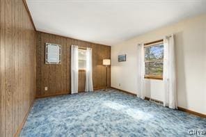 unfurnished room with carpet flooring, a wealth of natural light, and wood walls