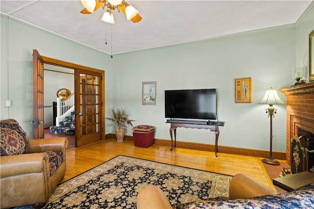 living room with ceiling fan, hardwood / wood-style floors, a fireplace, ornamental molding, and french doors