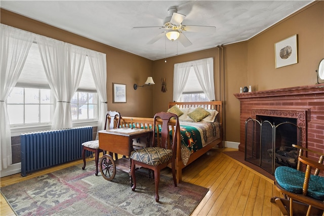 bedroom with wood-type flooring, a brick fireplace, radiator heating unit, and ceiling fan