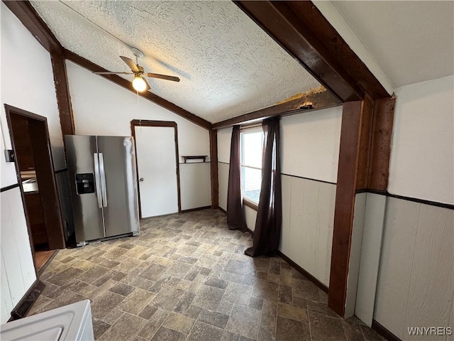 kitchen with wood walls, lofted ceiling with beams, ceiling fan, stainless steel refrigerator with ice dispenser, and a textured ceiling