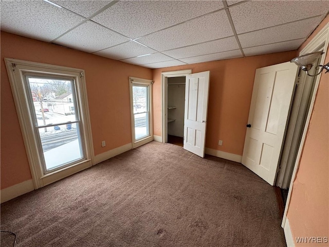 unfurnished bedroom featuring a drop ceiling and dark carpet