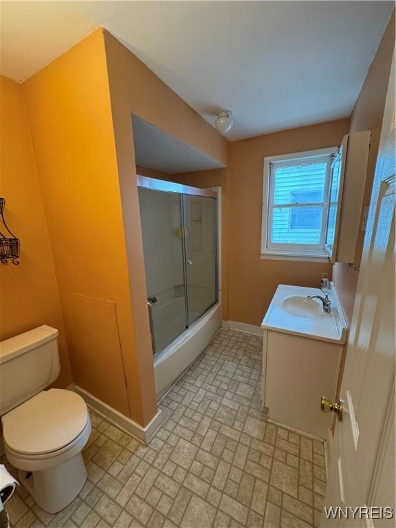 full bathroom with enclosed tub / shower combo, vanity, and toilet