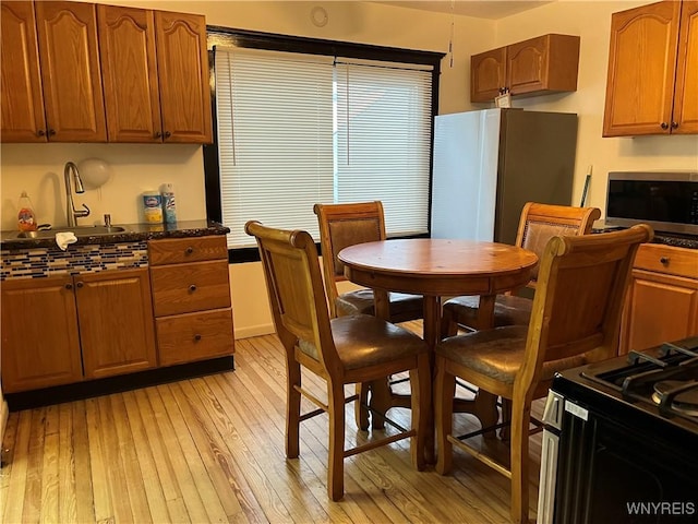 kitchen featuring appliances with stainless steel finishes, light hardwood / wood-style floors, sink, and dark stone countertops