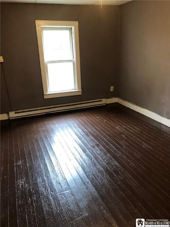 empty room featuring a baseboard heating unit and dark hardwood / wood-style flooring