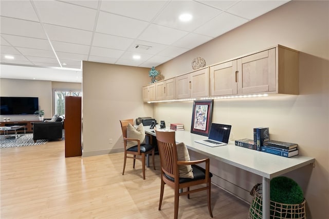 home office featuring a paneled ceiling, built in desk, and light hardwood / wood-style floors