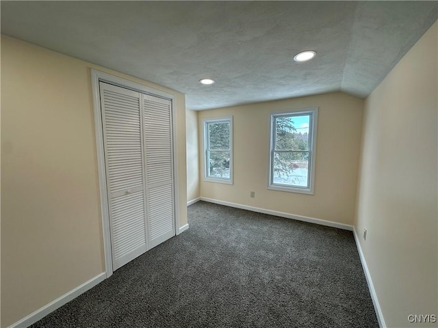 unfurnished bedroom featuring vaulted ceiling, a textured ceiling, dark carpet, and a closet