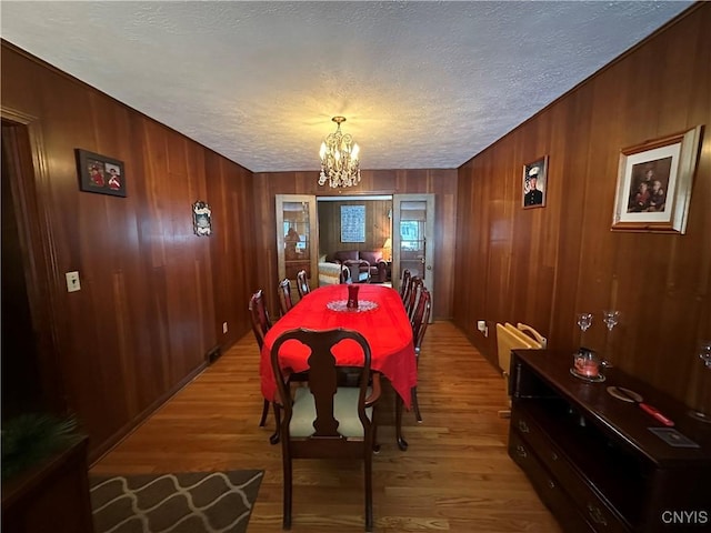 dining area featuring hardwood / wood-style flooring, wood walls, a textured ceiling, and a notable chandelier